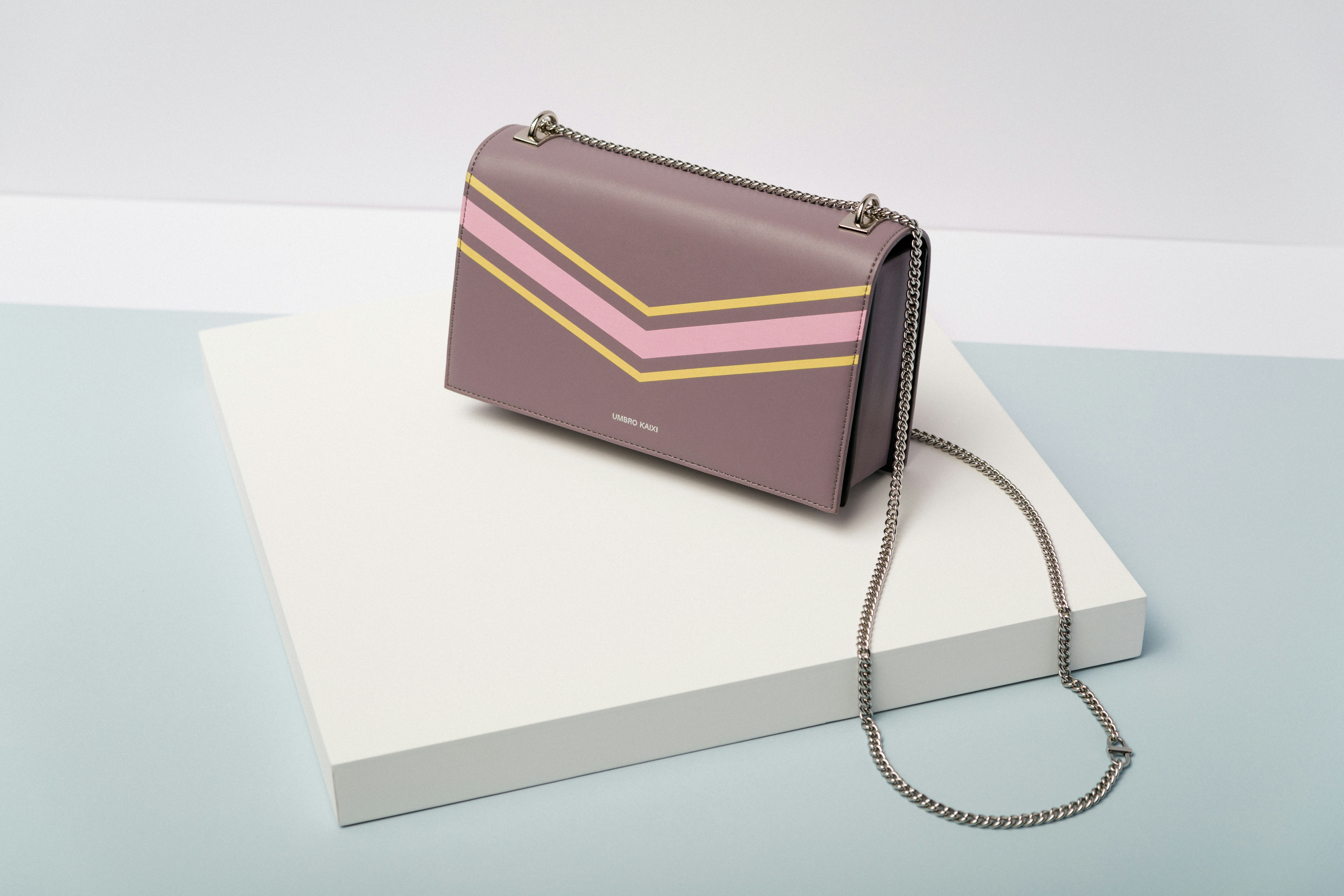 A brown/purple purse with yellow and pink stripes on it, and a silver chain